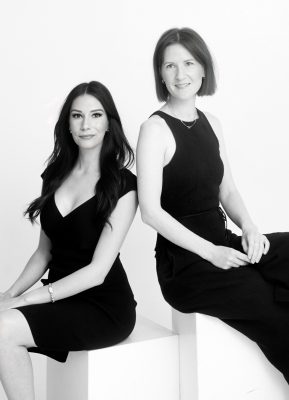 Two women in a black dress sitting side by side